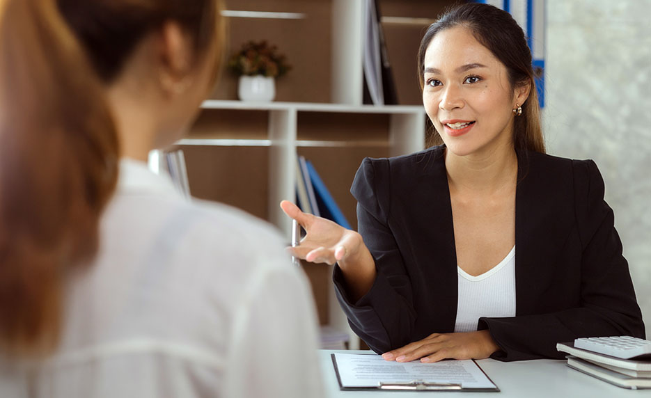 professional woman speaking to another at a desk