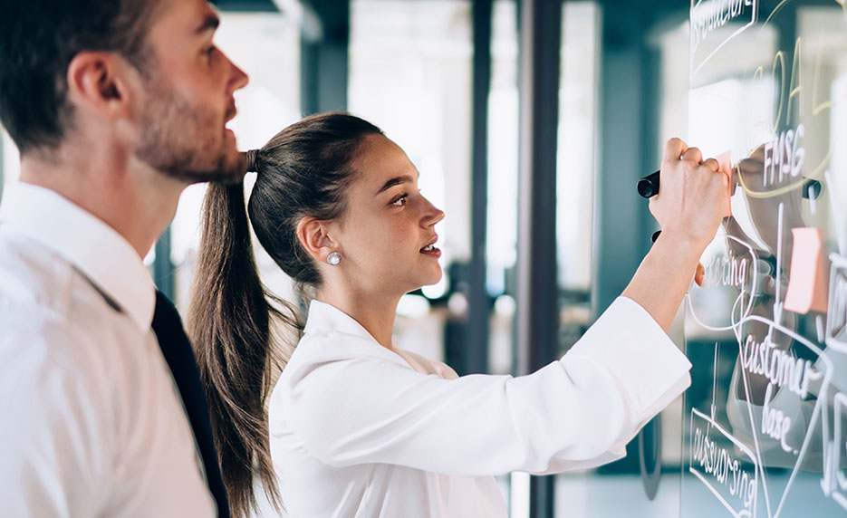 two professionals writing on a clear whiteboard