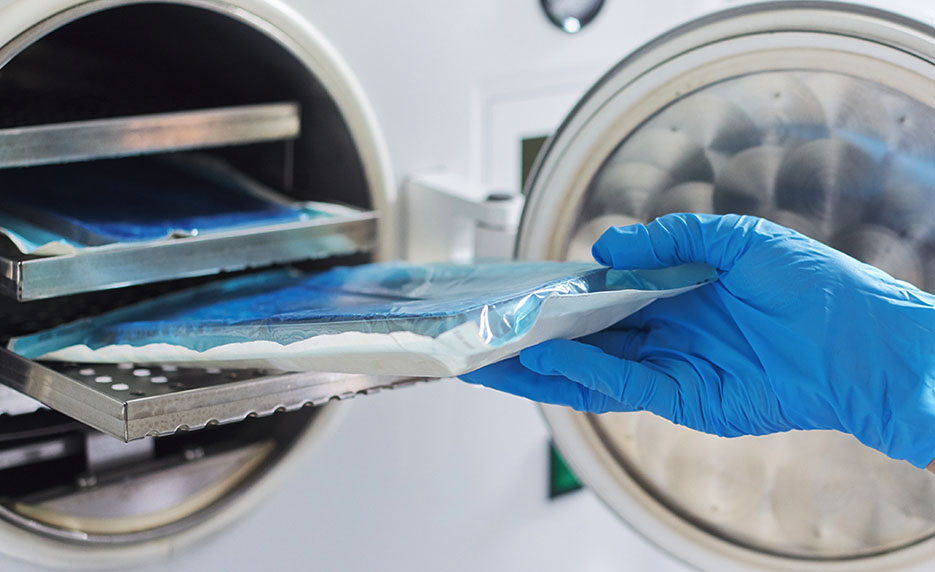 gloved hands putting a tray into a sterilizer